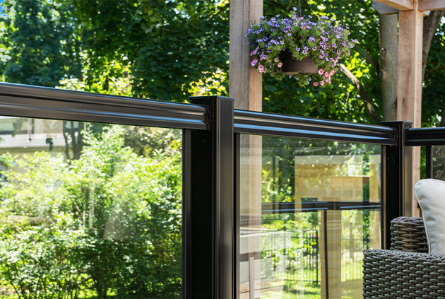 Black aluminum, glass deck railing, and beautiful landscape with hanging pot of flowers in the backyard.